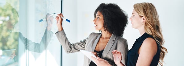 two women strategising whilst writing on a white board